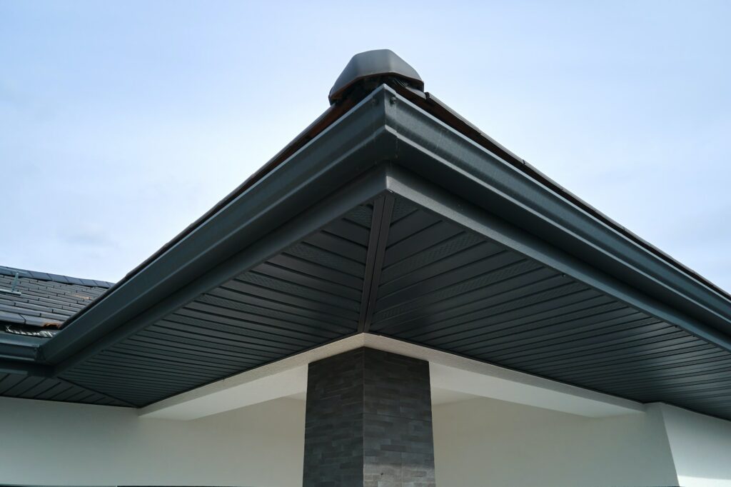 House corner with brown metal planks siding and roof with steel gutter rain system.